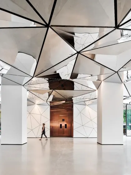 The expansive lobby space is defined by clean white columns that contrast with the complex, reflective ceiling. This design choice emphasizes the ceiling as the primary artistic feature of the interior.