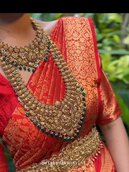 A close-up view of a traditional red bridal saree. This shot highlights the perfect fall of the pleats over the chest and the way the drape complements the heavy antique temple jewelry.