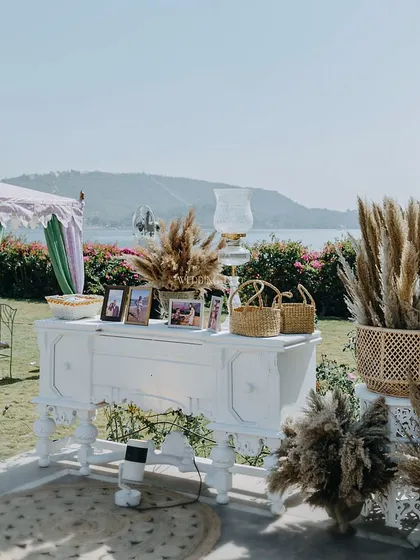 A memory station set against a stunning lakeside view. A vintage-style white console table was used to display the couple's photos, surrounded by pampas grass for a soft, romantic feel.