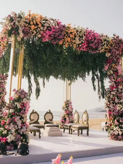 A close-up of the beach wedding mandap. The structure is lavishly decorated with pink, peach, and white flowers, with hanging greenery adding a touch of tropical charm.
