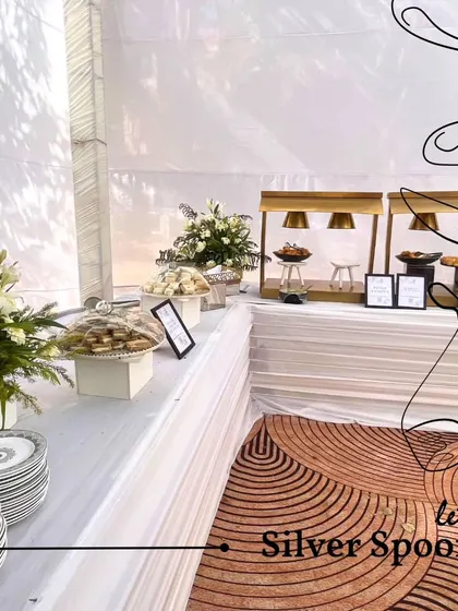 An elegant buffet line with white linens and floral arrangements. Our team ensures that every detail, from the plate settings to the food warmers, is perfectly in place.