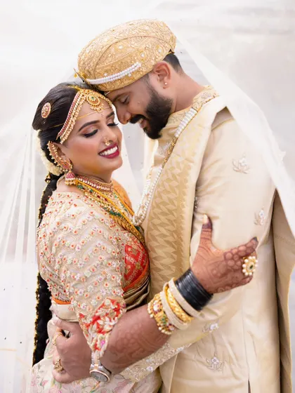 A truly radiant couple. I designed the groom's classic cream and gold silk outfit to complement the bride's vibrant red and gold wedding saree, creating a look that is both traditional and full of joy.