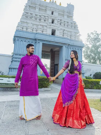 A vibrant and traditional pre-wedding look for a couple's shoot at a temple. She is wearing a custom red and purple half-saree, and he is in a matching purple kurta.