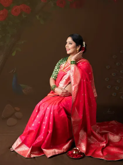 A moment of peaceful anticipation. Seated gracefully, this mom-to-be in her pink saree looks towards the future, surrounded by artistic elements like a peacock.