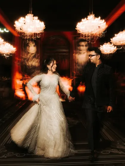 A creative motion-blur shot of the couple walking through a grand, chandelier-lit hall. The effect captures the whirlwind of emotion and movement during their Sangeet night.