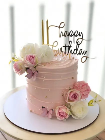 An elegant pink cake decorated with fresh flowers and edible butterflies.