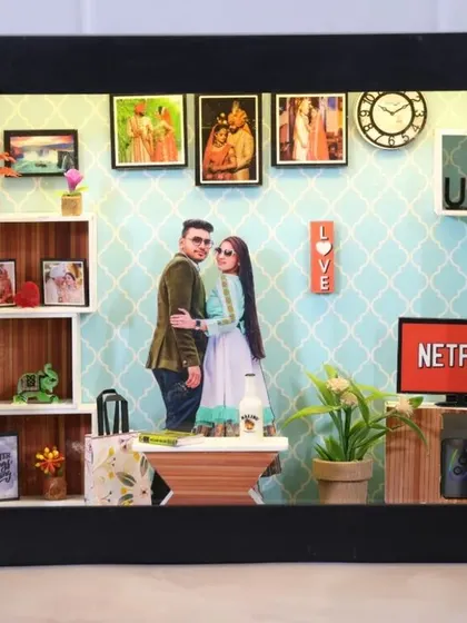 A cozy 'Netflix and chill' themed miniature box for a couple. It includes a mini TV with the Netflix logo, a comfy couch setup, and their photos.