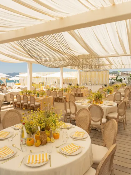 The dining setup for the Cannes Mehendi featured round tables with yellow and white striped linens, rattan chairs, and fresh yellow floral centerpieces, creating a cheerful, summery vibe.