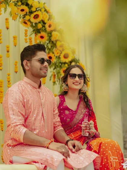 The couple looking cool and relaxed in sunglasses during their outdoor Haldi ceremony, set against a backdrop of sunflowers.