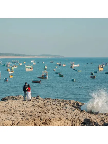 A stunning wide-angle shot of a couple standing on a rocky outcrop, surrounded by a sea full of colourful fishing boats.