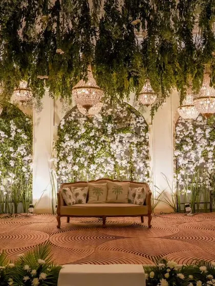 The stage is the heart of any reception. I designed this one with a ceiling of hanging greenery and crystal chandeliers above walls of white flowers, creating a lush, romantic backdrop for the couple.