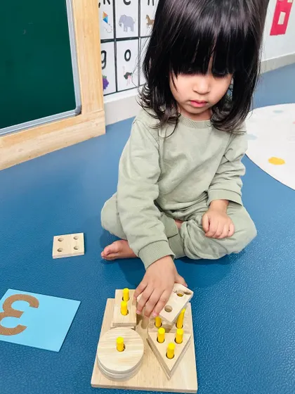 A toddler concentrates on placing pegs into a shape sorter, an activity that builds both numeracy and fine motor skills.