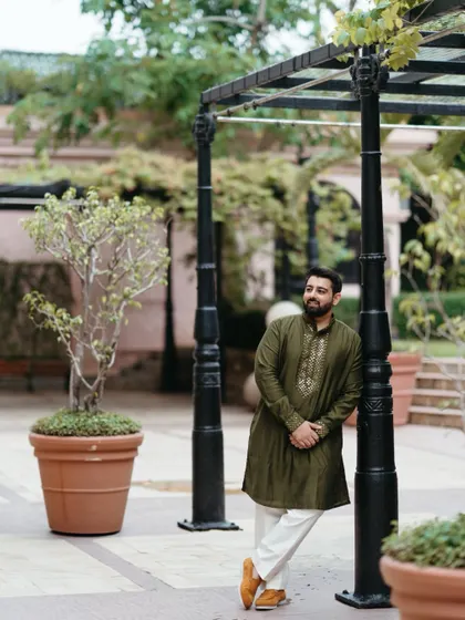 A relaxed portrait of the groom during the mehndi ceremony. Leaning against a post in a garden setting, he exudes a cool and casual confidence.