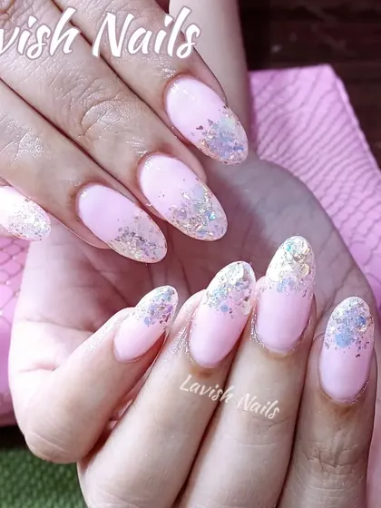 A glitter fade technique on acrylic nails, featuring iridescent flakes that catch the light beautifully against a soft pink base.