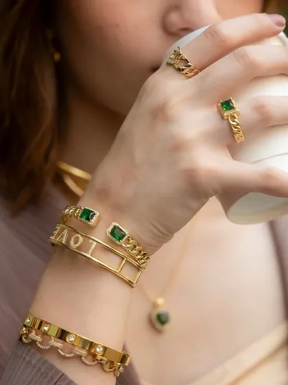 A close-up of a chic wrist stack, perfectly paired with a morning coffee. The emerald and gold tones create a look of effortless luxury.