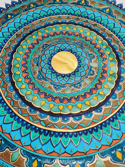 A macro shot of the center of the 'Peacock in the Desert Rain' mandala. You can see the layers of color and the metallic gold paint that gives the piece a warm glow.