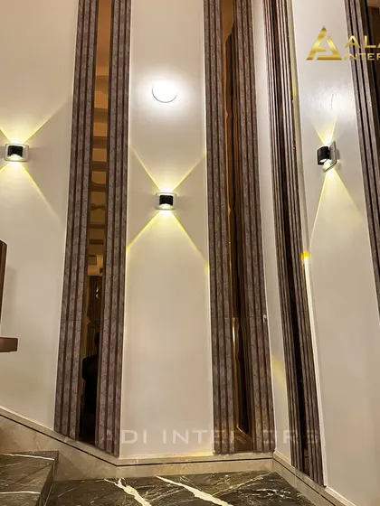 An elegant staircase wall treatment featuring vertical panels of wood and mirror, accentuated by modern, dual-direction wall sconces that create beautiful light patterns.