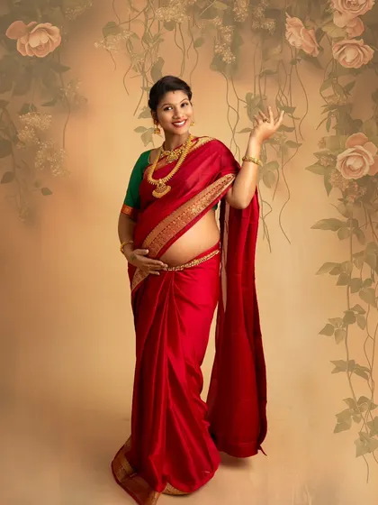 A stunning portrait of a mother-to-be in a vibrant red saree, showcasing her baby bump. The pose is confident and graceful, celebrating the beauty of her changing body.
