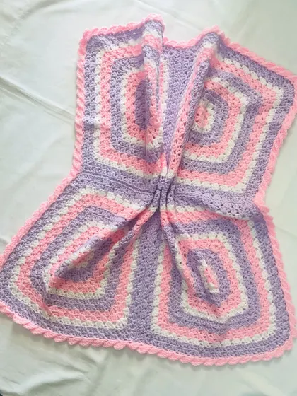 The soft folds of this pink and purple granny square blanket show how cozy and comfortable it is. It's lightweight enough for an AC room in the summer but warm enough for winter.