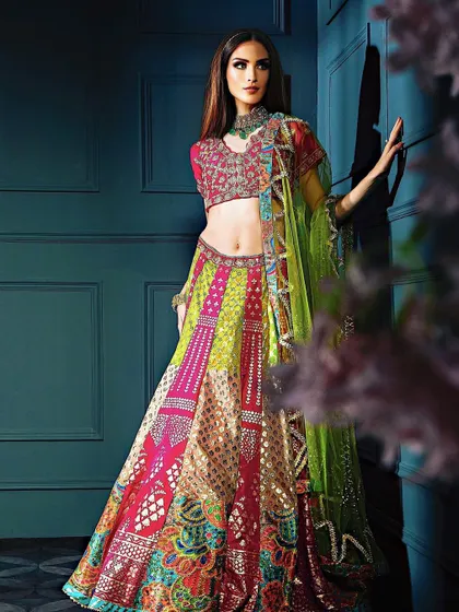 A full-length view of the vibrant multi-colored lehenga against a dark teal wall. The contrast makes the colors of the outfit pop, creating a visually striking fashion statement.