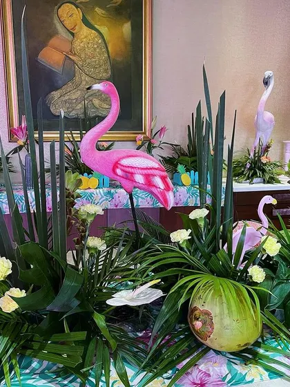 A long table decorated with a dense arrangement of tropical foliage, coconuts, and flamingo figures, creating an immersive jungle-like tablescape.