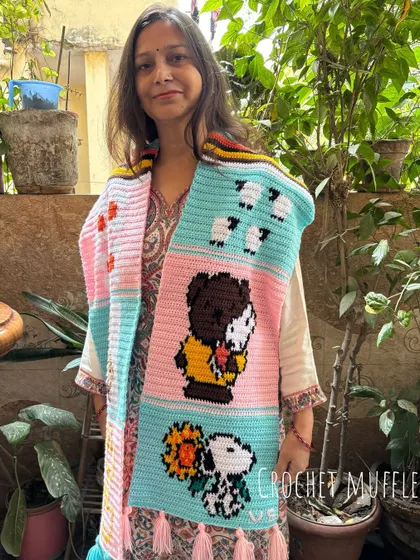 Here is my mom, Nirmala, proudly showing off a one-of-a-kind tapestry muffler we made for a customer. It features fun cartoon characters like Snoopy, sheep, and ducks, all hand-stitched with love. We can create a custom story just for you.