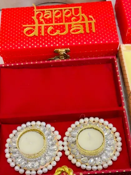 A close-up of a red 'Happy Diwali' box with pearl diya holders.