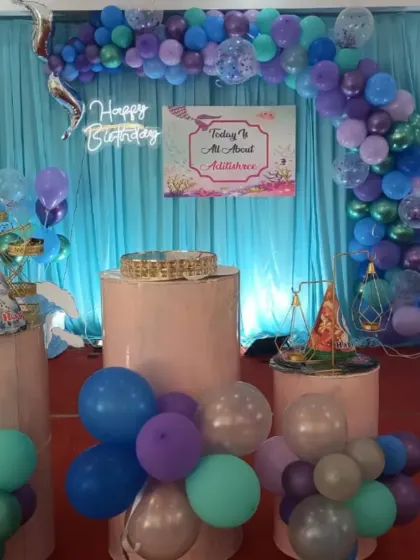 An under-the-sea mermaid theme brought to life with a palette of purple, blue, and teal balloons. The setup includes a custom backdrop, a 'Happy Birthday' neon sign, and themed dessert stands.