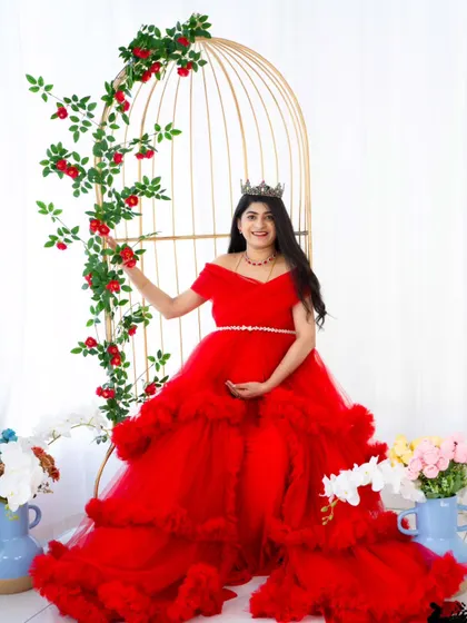 A fairytale moment in our studio. The mom-to-be stands in a vibrant red ruffled gown next to our decorative golden birdcage, creating a whimsical and enchanting scene.