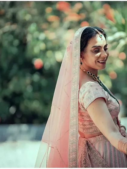 A beautiful, soft-focus portrait of a bride in a pastel pink lehenga, her gentle smile and flowing dupatta creating a dreamy and elegant look.