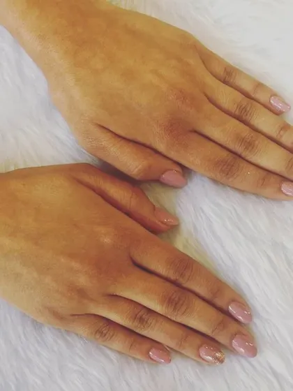 A perfect example of subtle elegance. These short, natural nails are painted in a soft nude pink, with a hint of gold glitter on the accent nail for a delicate touch of glam.