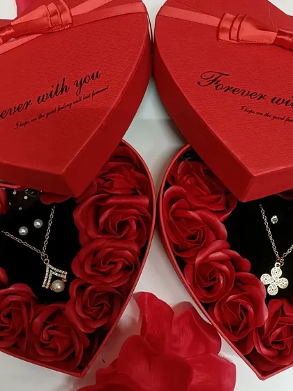 We have different necklace designs available in our heart-shaped gift boxes. Here you can see two options, one with a pearl and the other with a four-leaf clover design.