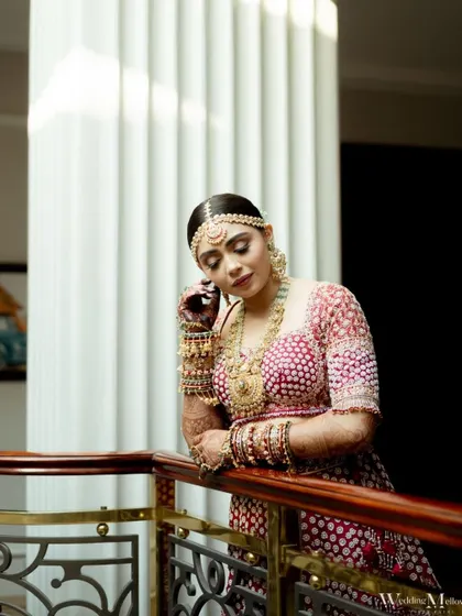 The bride leans against a balcony railing, a picture of grace and elegance. This portrait captures a quiet moment of reflection on her special day.