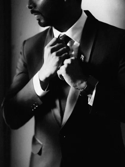 A moody, artistic black and white shot of the groom adjusting his tie, a classic moment of preparation and anticipation.
