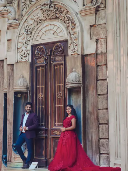 A classic pre-wedding couple pose against a grand, European-style door set. The maroon red gown adds a touch of romance and drama.