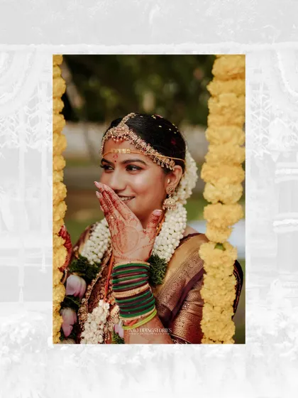 A beautiful portrait of a smiling South Indian bride, framed by marigold garlands, capturing a moment of quiet joy.