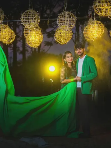An evening shot of a couple in coordinated green outfits. The flowing trail of the gown and the dramatic lighting create a magical, cinematic effect.