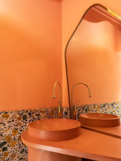 A close-up of the pink powder room highlights the custom-made concrete basin. Its color perfectly matches the pedestal and walls, creating a monolithic effect. The terrazzo and brass faucet add layers of texture and refinement.