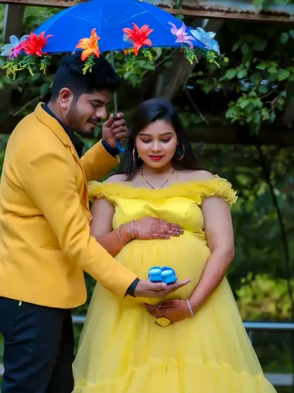 A playful maternity photo with the father-to-be holding a floral umbrella over his partner, who is glowing in a yellow gown.