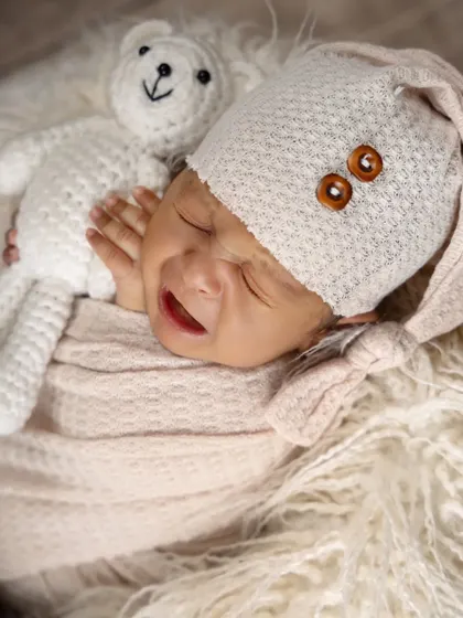 Capturing the real moments, including a little cry. This newborn, dressed in a cozy hat and swaddle, shows a fleeting expression while snuggling a teddy bear.