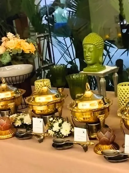 A buffet table featuring a mix of modern and traditional elements. Polished brass serving dishes are set alongside contemporary bowls and decor pieces like a Buddha head statue, creating a unique, eclectic look.
