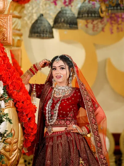 A glamorous bridal portrait. The bride, in her rich red lehenga, poses against a backdrop of ornate, traditional decor.