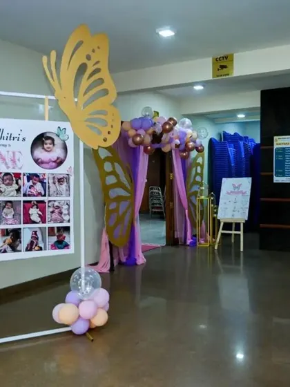 A welcome area featuring a milestone photo board for Adhitri's first birthday. The large butterfly cutouts tie it into the overall party theme.
