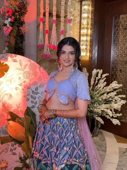 A vibrant and fun Mehendi look. The bride's hair is styled in a playful, textured braid that complements her colorful outfit and the festive atmosphere.