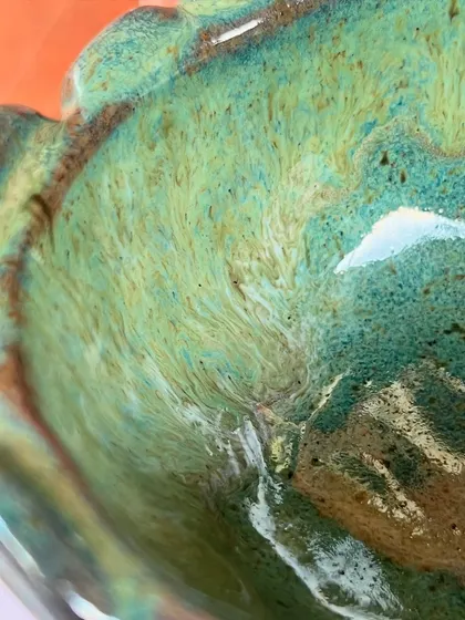 A close-up of the beautiful marbled glaze inside a bowl made by a student. The swirling greens and browns create a dynamic, earthy effect.