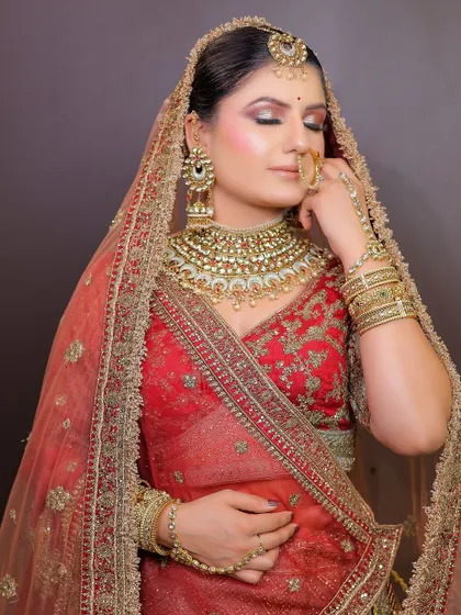 A beautiful bride in a red and gold lehenga with a sheer dupatta. This look is a testament to timeless bridal elegance, available for rent along with the jewellery.
