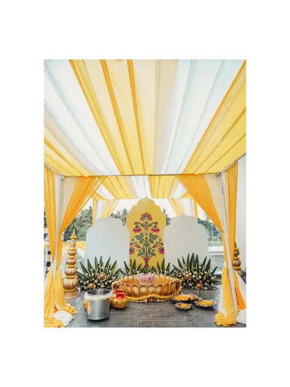 A shot of the beautiful Haldi decor, featuring a yellow and white tent and a floral backdrop, setting the stage for the celebration.