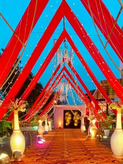 An outdoor entrance defined by bold red fabric drapes forming a triangular tunnel. This design is simple yet powerful, creating a striking visual against the evening sky.
