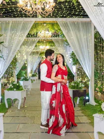 We love creating magical settings for your sangeet or reception. This couple is framed by a romantic walkway of draped white fabric, sparkling fairy lights, and elegant chandeliers, perfect for an evening of dance and celebration.