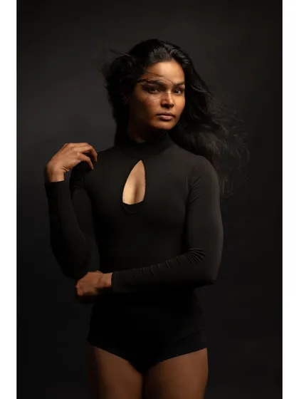 A minimalist and contemplative fine art portrait. The simple black bodysuit and dark background, combined with the motion of the hair, create a sense of quiet introspection.